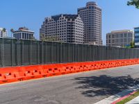 an orange barrier beside the road with buildings in the background and some blue skies behind it