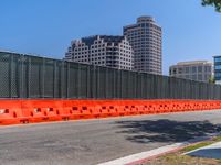 an orange barrier beside the road with buildings in the background and some blue skies behind it