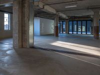 a room with some concrete flooring and large windows with lights coming through it on one side and an open ceiling above the rest of the other