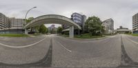 a curved city street with buildings in the background and a bridge above it with the road running parallel