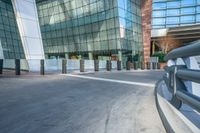 an empty concrete and brick walkway leading to an glassy building, in front of a sidewalk