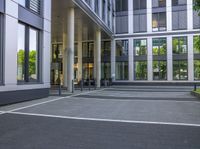 a street with an empty walkway lined with tables and chairs and trees outside building with large glass windows