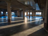 an empty industrial building is pictured lit from inside by bright light that is partially covered by columns