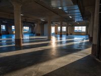 an empty industrial building is pictured lit from inside by bright light that is partially covered by columns