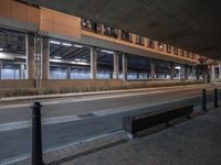 a bench sitting on the curb by a parking garage and walkway at night, in front of an empty building