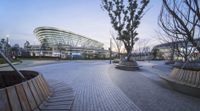 a circular city park with benches in the foreground, with large buildings and trees on each side