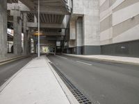 empty road under overpass at city street with buildings in background next to road under bridge