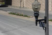 a metal street light on the side of a street next to a road and a brick building