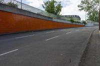 a city street with an orange wall on it and a concrete road lined by trees