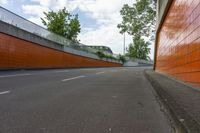 a city street with an orange wall on it and a concrete road lined by trees