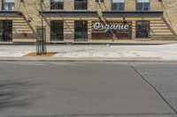 a street with an empty sidewalk and an outside building with a sign on it that says organic