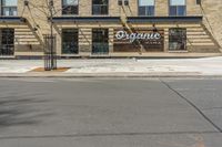 a street with an empty sidewalk and an outside building with a sign on it that says organic