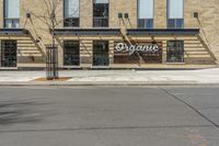 a street with an empty sidewalk and an outside building with a sign on it that says organic