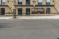 a street with an empty sidewalk and an outside building with a sign on it that says organic