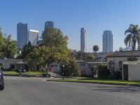 a street with cars driving by buildings and palm trees in the background and people walking down the street