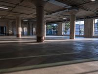 empty industrial warehouse with concrete pillars and open floor plans and windows overlooking trees and tall buildings