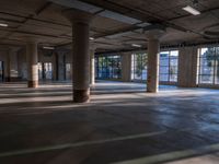 empty industrial warehouse with concrete pillars and open floor plans and windows overlooking trees and tall buildings