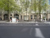 trees and benches along an asphalt road in front of a tall building with arched windows