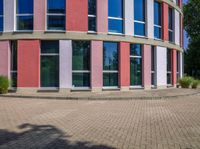 a building with several stories reflecting in the windows and the circular bricked walkway outside