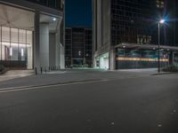 an empty street with a lit up building on the other side of the road near the intersection of two large buildings