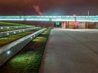 an outside area with a clock and green grass in the ground with lights illuminating up