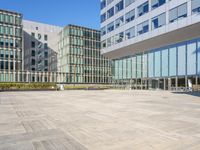 a paved area with a bench and glass building in the background, there are several buildings and a clear blue sky