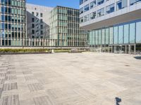 a paved area with a bench and glass building in the background, there are several buildings and a clear blue sky