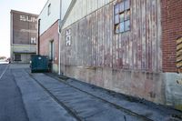 an empty street has graffiti on the side of buildings and a dump can near by