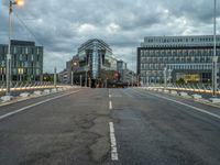 an empty road with some modern buildings in the back ground and a red traffic light at the top