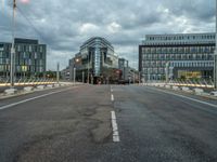 an empty road with some modern buildings in the back ground and a red traffic light at the top