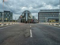 an empty road with some modern buildings in the back ground and a red traffic light at the top