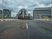 an empty road with some modern buildings in the back ground and a red traffic light at the top