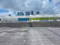 a large parking lot with some buildings behind it and clouds overhead above it in a city