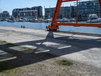 large red truss frame by the water with some docked boats in the background with people walking on walkway