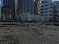 the truck is parked on the asphalt with the buildings in the background and a train going by