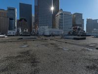 the truck is parked on the asphalt with the buildings in the background and a train going by