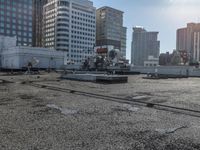 the truck is parked on the asphalt with the buildings in the background and a train going by