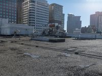 the truck is parked on the asphalt with the buildings in the background and a train going by