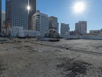 the truck is parked on the asphalt with the buildings in the background and a train going by