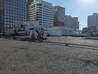 the truck is parked on the asphalt with the buildings in the background and a train going by