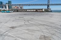 an empty parking lot with car tires painted on it and a boat dock in the back ground