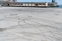 an empty parking lot with car tires painted on it and a boat dock in the back ground