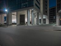 an empty street in the center of a city at night, with a large building in the background