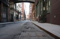 an alley way with people walking along and two cars in the street and buildings behind