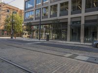 a car driving down a street next to tall buildings with trees in the background and on the pavement, an electric tram track goes to right