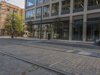 a car driving down a street next to tall buildings with trees in the background and on the pavement, an electric tram track goes to right