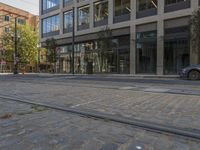 a car driving down a street next to tall buildings with trees in the background and on the pavement, an electric tram track goes to right