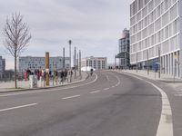 a group of people standing on the side of a road next to tall buildings and trees