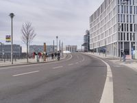 a group of people standing on the side of a road next to tall buildings and trees