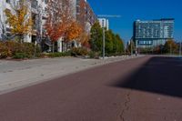 a sidewalk with a bus stop sign next to some buildings and trees with leaves growing on them